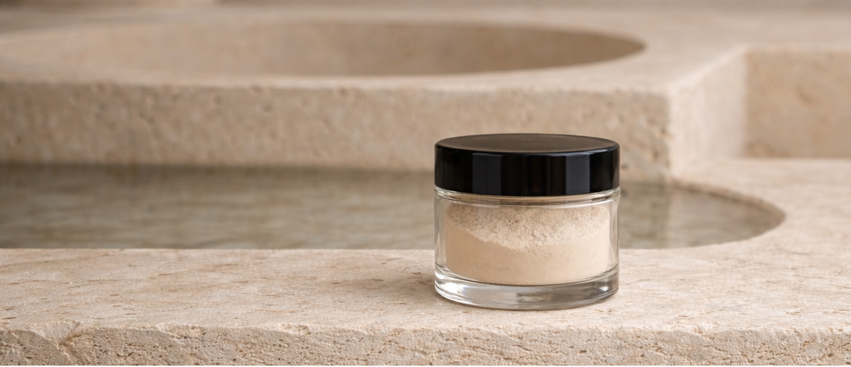glass jar of Katharos Hydroxyapatite Toothpowder on honed travertine surface