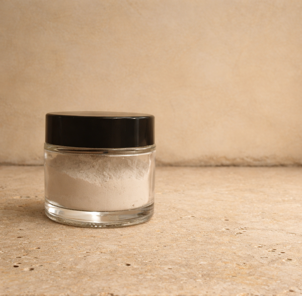 Clear jar of hypdroxyapatite toothpowder with black lid on a travertine surface